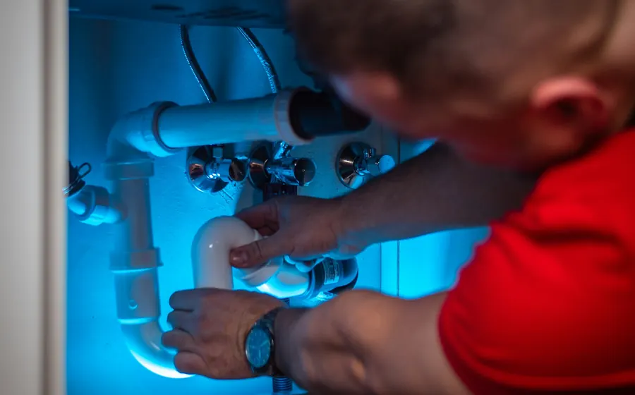 Técnico reparando una cañería bajo un mueble de cocina